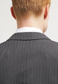Grau kariertes Anzugjackett mit strukturierter Silhouette, das einen weißen Kragen und saubere Nähte entlang der Nähte aufweist.