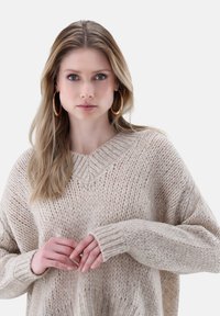 Beige gestrickter Pullover mit V-Ausschnitt und gerippten Bündchen, mit lockerer Passform und weichem Textur. Glattes Garn mit subtilen Farbvariationen.