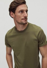 Olivgrön t-shirt med rund halsringning, korta uppvikta ärmar, tillverkad av slätt bomullstyg. Enkel design utan mönster eller synliga detaljer.