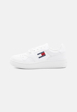 Witte sneaker gemaakt van glad leer met een gewatteerde boord en tong, geperforeerde neus en een decoratieve logopatch in rood, wit en blauw.