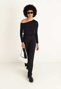 Fekete off-shoulder felső redős textúrával, laza fekete nadrággal és platform fekete csizmával párosítva. Egy ezüst kézitáska és napszemüveg egészíti ki a megjelenést.