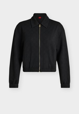 Μαύρο μακρυμάνικο τζάκετ με φερμουάρ, γιακά, ελαστικά μανσέτες και τελείωμα, διακριτικό ανάγλυφο μοτίβο και χρυσό τράβηγμα φερμουάρ κλειστό μπροστά.