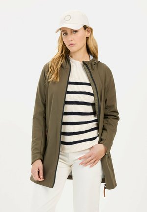 Olive green lightweight jacket with a zippered front, paired with a cream and navy striped sweater and beige pants. White cap with logo.