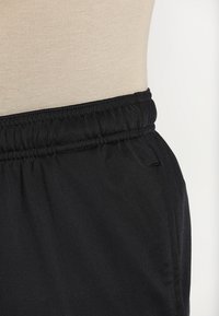 Gros plan sur une ceinture élastique noire d'un pantalon présenté sur un buste de mannequin beige sur fond blanc.