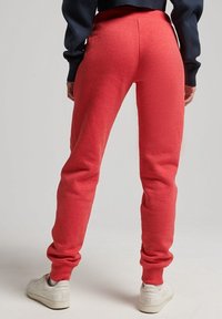 Person wearing red sweatpants and white sneakers standing against a neutral background, hands relaxed by sides.