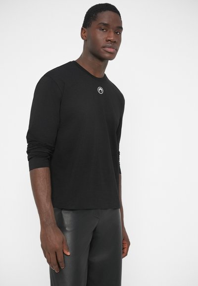 Camisola preta de mangas compridas com decote redondo e pequeno logótipo circular no peito. O tecido parece liso, com um corte ajustado.