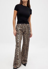 Top negro de manga corta combinado con pantalones de pierna ancha de estampado de leopardo, hechos de tela texturizada, que presentan patrones en diferentes tonos de marrón y negro.