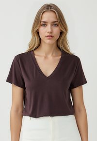 T-shirt marrone a scollo a V realizzato in tessuto morbido, con maniche corte e una vestibilità rilassata, abbinato a pantaloni bianchi a vita alta.