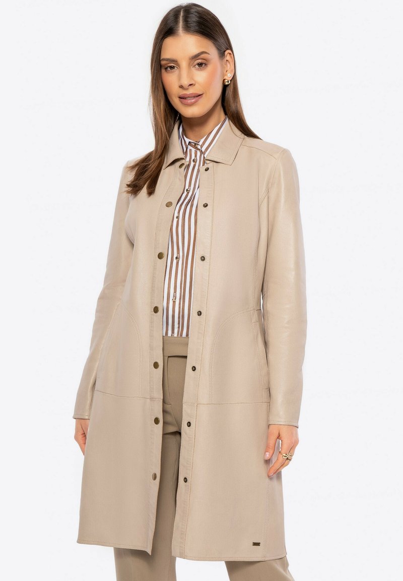 Beige leren jas met knopen aan de voorkant, lange mouwen, zijzakken en een getailleerd ontwerp. Gecombineerd met een gestreepte shirt eronder.