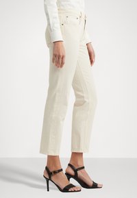 Beige rechte jeans met zijzakken en een hoge taille, gecombineerd met zwarte strappy hakken met een dunne hak en enkelbandje.