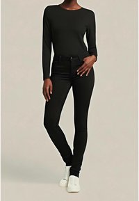 Haut noir à manches longues associé à un jean noir ajusté en tissu stretch. Comprend un col rond et des baskets blanches à finition texturée.