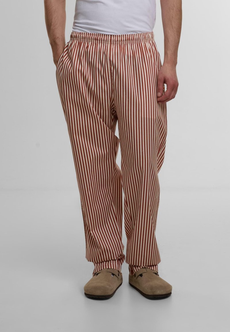 Pantaloni ușori cu dungi în nuanțe de bej și roșu, având un talie elastică și buzunare laterale, asortați cu cizme slip-on de culoare maro deschis.
