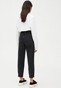 Pantalon en denim noir fuselé avec une taille haute élastique, présentant des revers retroussés. Porté avec une chemise blanche à manches longues et des baskets noires.