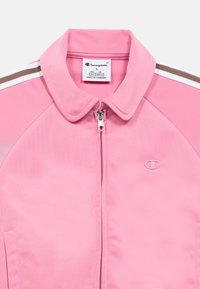 Ανοιχτό ροζ αθλητικό μπουφάν με φερμουάρ, ριμπ γιακά και λευκές και καφέ ρίγες στους ώμους. Διαθέτει κεντημένο λογότυπο στο στήθος.