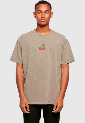 Brown, oversized t-shirt made of cotton, featuring a small red and green cherry print on the chest. Short sleeves and round neckline.