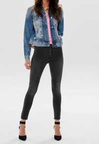 Blå denimjacka med knäppning och fickor, kombinerad med högmidjade mörkgrå smala jeans och svarta klackskor med ankelremmar.