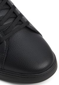 Černé kožené tenisky s texturovaným povrchem, kulatou špičkou a plochými tkaničkami. Mají pevnou gumovou podrážku a minimalistické designové detaily.