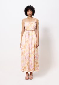 Robe maxi florale dans des nuances de rose et de jaune, avec des bretelles fines et une taille cintrée. Complétée par des sandales roses à lanières.