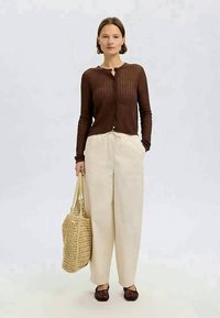 Καφέ ριμπ πουλόβερ, μπεζ παντελόνι με κορδόνι, υφασμάτινη τσάντα από ψάθα και σκούρα καφέ παντόφλες. Απλή, χαλαρή εφαρμογή με υφασμάτινη υφή.