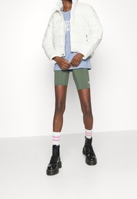 White puffer jacket, light blue t-shirt with logo, olive green shorts, black lace-up boots, and white socks with pink stripes.