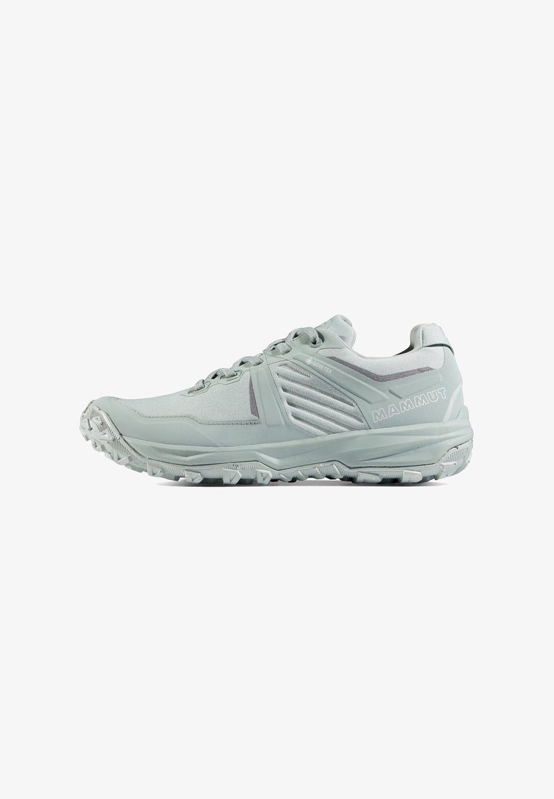 Chaussure de randonnée gris clair avec semelle robuste, lacets et logo Mammut sur le côté, conçue pour un usage extérieur.