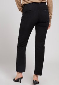 Pantaloni in denim nero con una silhouette aderente, caratterizzati da una vita alta, tasche posteriori discrete e un design a gamba dritta. Texture liscia e dettagli minimi.