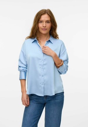 Light blue, long-sleeve shirt with a button front, oversized fit, and a classic collar. Soft fabric and rolled cuffs complement denim jeans.