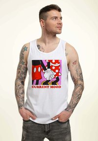 Camiseta sin mangas blanca con personajes de dibujos animados cogidos de la mano, combinada con un vestido de lunares rojos y blancos y pantalones cortos negros. El texto debajo dice "ESTADO ACTUAL".