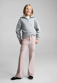 Sivá mikina s vysokým golierom a polovičným zipsom, skombinovaná so svetloružovými cargo nohavicami. Čierne baleríny dotvárajú outfit.