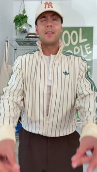Jonge man die een wit krijtstreep jasje en een beige pet draagt, knipogend voor een plank met planten en een groen bord met de tekst "COOL PEOPLE."