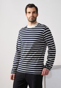 Marineblau-weiß gestreiftes Langarmshirt mit Rundhalsausschnitt; weicher Stoff; mit kontrastierendem Rippkragen und enganliegenden Bündchen.