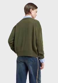 Olivově zelený pletený svetr s volným střihem, ribovanými manžetami a designem s kleslým ramenním, vrstvený přes světle modrou pruhovanou košili.