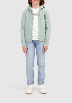 Lichtgroene rits-hoodie met een gladde stof, voorzien van een capuchon met trekkoord en logo-detail. Gepaard met een wit T-shirt en blauwe spijkerbroek.