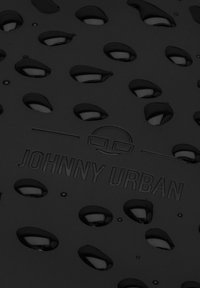 Suprafață texturată neagră cu decupaje ovale și mici picături de apă. Numele mărcii "JOHNNY URBAN" este gravat cu litere îngroșate.