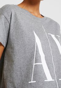 Camiseta de algodón gris con un gran estampado gráfico blanco, de manga corta y un corte relajado. La tela tiene una textura suave.