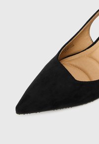 Črne semiš čevlje s koničastim nosom in izrezanimi stranicami ter oblazinjenim vložkom. Podplat ima majhne gumijaste izbokline za oprijem.