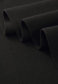 Tissu tricoté noir avec une surface texturée, comportant plusieurs couches pliées qui mettent en valeur sa matière douce et chaude.