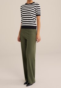 Randig kortärmad topp i svart och vitt, kombinerad med högmidjade olivgröna vida byxor och svarta spetsiga skor.