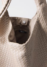 Beige gewebte Handtasche mit strukturiertem Äußeren und glattem Innenfutter. Mit Druckknopfverschluss und einer kleinen Reißverschlusstasche im Inneren.