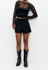 Czarna przezroczysta bluzka z długim rękawem i dekoltem w łódkę, zestawiona z czarnymi szortami z wysokim stanem. Do tego czarne kowbojki sięgające do kolan.