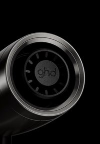 Gros plan sur une buse cylindrique noire de sèche-cheveux avec le logo "ghd" à l'intérieur, sur un fond noir uni.