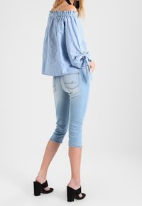 Blau-weiße gestreifte Off-Shoulder-Bluse mit Schleifenärmeln, kombiniert mit hellblauen Skinny-Jeans und schwarzen High-Heels.