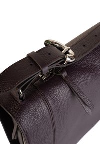 Bolso de mano de cuero púrpura con una superficie texturizada, herrajes en plata, correa ajustable y detalles decorativos de cuero.