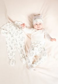 Dwuczęściowy strój dla niemowląt składający się z body z długim rękawem i spodni, oba w jasnokremowym kolorze z czarnymi wzorami zwierząt; zawiera dopasowaną czapkę.