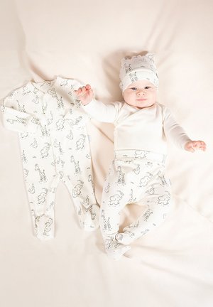 Dwuczęściowy strój dla niemowląt składający się z body z długim rękawem i spodni, oba w jasnokremowym kolorze z czarnymi wzorami zwierząt; zawiera dopasowaną czapkę.