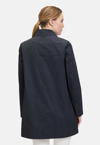 Marineblauer wasserdichter Mantel mit kragenförmigem Ausschnitt, geradem Schnitt und langen Ärmeln. Hergestellt aus einem leichten, glatten Material.