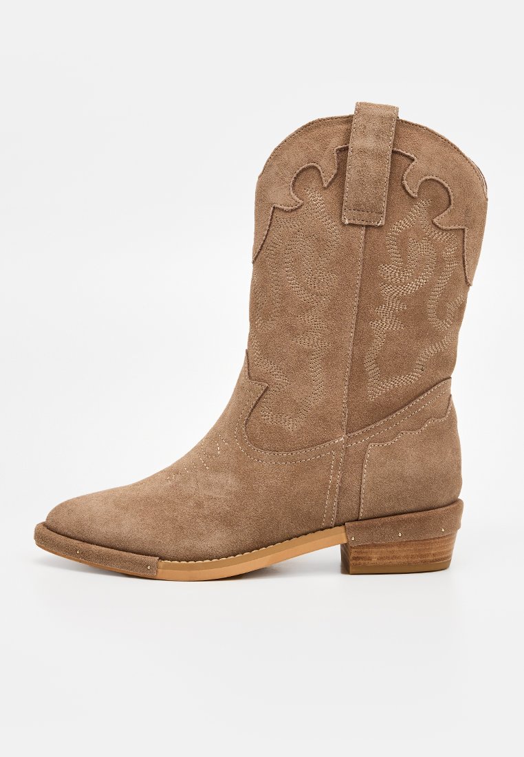 Bota de vaquero marrón de ante con puntera puntiaguda, detalles texturizados, costuras decorativas y tacón bajo apilado. No presenta adornos.