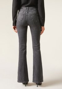 Jean en denim noir évasé avec une taille haute. Dispose de deux poches arrière et d'une silhouette ajustée aux hanches, se transformant en une jambe plus large.