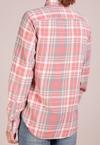 Långärmad rutskjorta med mönster i rosa, grå och vit, tillverkad i mjukt material med en rundad nederkant och knappdetaljer vid ärmsluten.