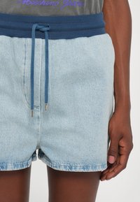 Lys blå denim-shorts med en ribbet marineblå linning og matchende snøring, med sølvfargede metalender og en avslappet passform.